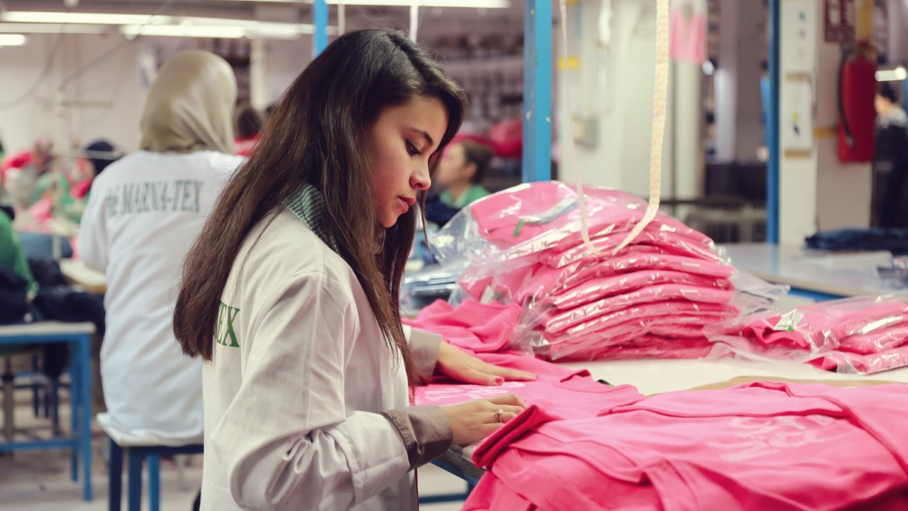 A young woman works and examines pink T-shirts.