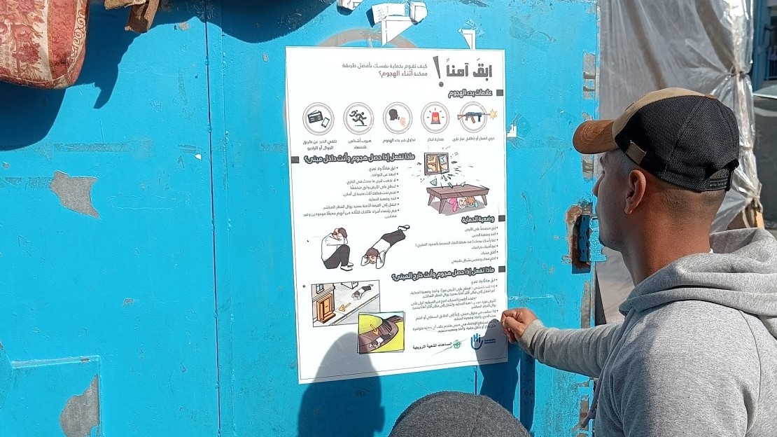 HI is putting up posters in camps for displaced people, explaining how best to protect oneself in the case of bombings and shellings, Khan Younis, Gaza Strip. 